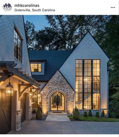 a large house with lots of windows and lights on it's front door, in the evening