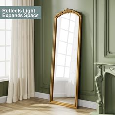 a large gold framed mirror sitting on top of a wooden floor next to a window