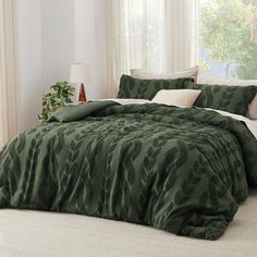 a bed with green comforter and pillows in a room next to a lamp on a table