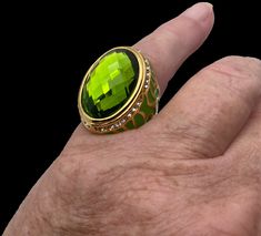 Wow! What a statement ring. This vintage ring has a large green either rhinestone or glass stone in the center surrounded by dainty white simulated diamonds on a 316L stainless steel which is the highest quality for jewelry. The band is then clothed in a gold tone overlay. The sides are decorated in green flames giving this ring more character, this is a very interesting piece of vintage costume jewelry. The size is 7.75 Elegant Green Oval Enamel Ring, Green Oval Enamel Ring For Formal Occasions, Green Oval Enamel Ring For Anniversary, Formal Green Oval Enamel Ring, Formal Oval Green Enamel Ring, Green Oval Enamel Anniversary Ring, Oval Green Enamel Anniversary Ring, Oval Green Enamel Ring Gift, Elegant Green Crystal Ring With Metal Band