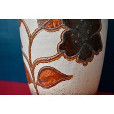 a white vase with orange and brown designs on it's sides, sitting on a red surface