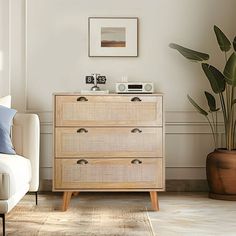 a living room with a white couch and a wooden dresser next to a potted plant