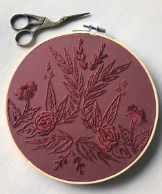 a pair of scissors sitting on top of a table next to a embroidery hoop with flowers