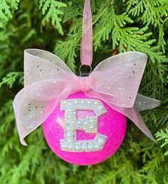 a pink ornament hanging from a tree with a bow and letter e on it