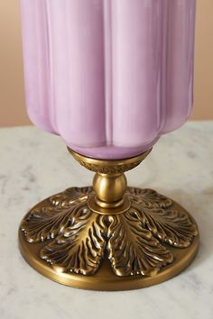 a purple vase sitting on top of a white table next to a gold candle holder