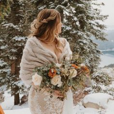 a woman standing in the snow holding a bouquet and looking out at mountains behind her