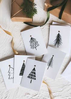 four cards with christmas trees drawn on them next to some wrapping paper and twine