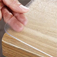 a hand holding a piece of clear plastic on top of a wooden table with wood grained edges