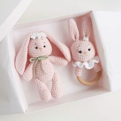 two pink crocheted stuffed animals in a white box with a wooden ring on it