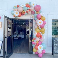 an entrance to a restaurant with balloons and flowers on the front door, decorated in pastel colors