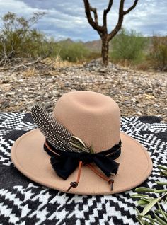 This tan felt hat is complimented with a rugged black band and a rust leather tie. It is accented with brass and carved bone beads and a turkey feather and dried olive leaves.  Wander in the desert. Rustic Brown Hat Bands For Fall, Bohemian Brown Hat For Outdoor, Southwestern Brown Feather Hat Bands, Southwestern Brown Hat Bands With Feathers, Rustic Adjustable Hats For Fall, Brown Hat Bands With Feathers For Western-themed Events, Feather Hat Bands For Western-themed Fall Events, Brown Hat Bands With Feathers For Western Events, Artisan Adjustable Fedora For Fall