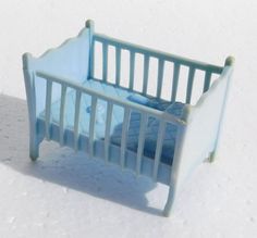 a toy crib sitting in the snow on top of a white surface with blue sheets