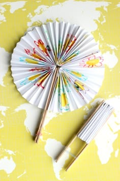 a paper fan with paint splattered on it next to two chopsticks