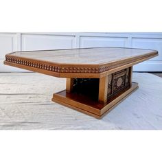 a wooden table with an intricate design on it's top and bottom edge, sitting in front of a garage door