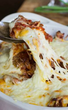 a white bowl filled with lasagna covered in cheese and meat, topped with a spoon