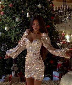 a woman standing in front of a christmas tree wearing a dress with long sleeves and sequins