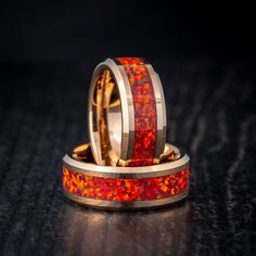 two wedding bands with red and yellow flowers inlayed to each other on a black surface