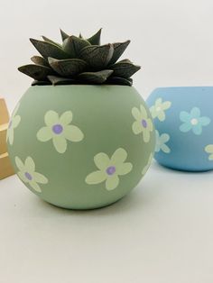 two vases with flowers painted on them sitting next to each other, one blue and one green