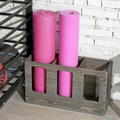 three pink yoga mats in a wooden crate next to a white brick wall and black rack