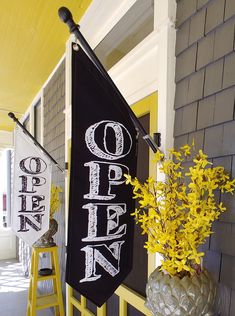 a black and white sign hanging from the side of a house next to yellow flowers