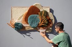 a man is working on an art work that looks like rugs and flowers hanging on the wall