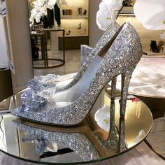 a pair of silver high heels sitting on top of a glass table in a store