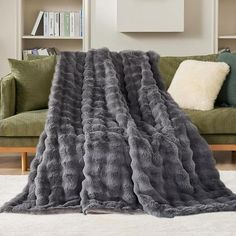 a large gray fur blanket sitting on top of a white rug next to a green couch