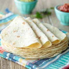 a stack of tortillas sitting on top of a table next to a bowl of salsa