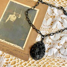 an old photo is attached to a chain on top of a lace doily with a black pendant