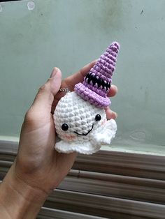 a hand holding a small crocheted unicorn toy with a purple hat on it's head