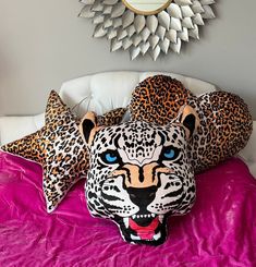 a leopard pillow sitting on top of a bed next to two pillows with blue eyes