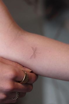 a woman's arm with a small dragonfly tattoo on it