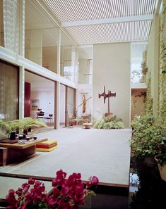 the inside of a house with plants and flowers on the outside floor, and an iron cross in the center