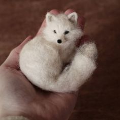 a hand holding a tiny white animal in it's palm