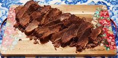 sliced beef on a wooden cutting board with floral table cloth and blue flowered napkin