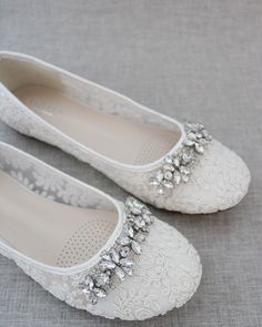 white wedding shoes with crystal embellishments on the toe and bottom are sitting on a gray surface