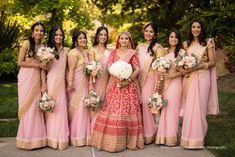 a group of women standing next to each other in front of trees and bushes with bouquets