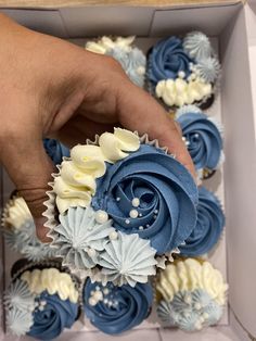 a person is holding a blue and white cupcake in a box with other cupcakes