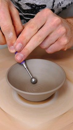 a person working on a pottery bowl with a small metal object in front of it