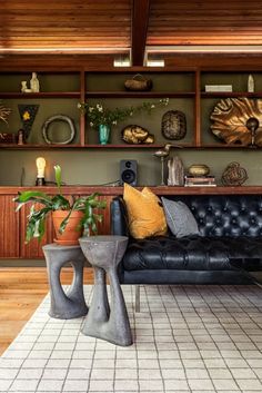 a living room with black leather furniture and wooden shelves on the wall, plants in vases