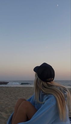 a woman sitting on top of a beach next to the ocean under a blue sky