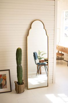 a large mirror sitting on the side of a wall next to a potted cactus