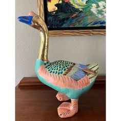 a duck statue sitting on top of a wooden table next to a painting and framed artwork