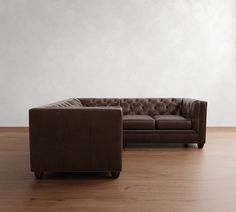 a brown leather couch sitting on top of a wooden floor next to a white wall