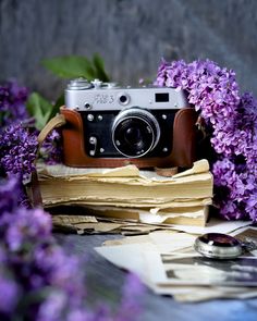 a camera sitting on top of a pile of paper next to purple flowers