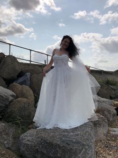 a woman in a white wedding dress standing on rocks with her arms around her waist