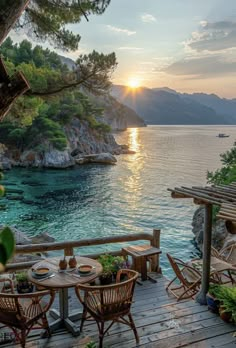 an outdoor dining area overlooking the water and mountains at sunset with wooden tables and chairs