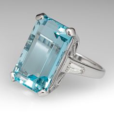 This stunning cocktail ring is centered with an emerald cut aquamarine, weighing 13.73 carats, in a four-prong setting. The shoulders are each two-prong set with one (1) tapered baguette cut diamond. The ring measures 19.5mm at the top, rises 10.8mm above the finger, tapering to 2.0mm wide and 1.2mm thick at the base of the shank. It is currently a size 7. Modern Formal Topaz Ring With Rectangular Stone, Modern Topaz Ring With Rectangular Stone For Formal Occasions, Formal Emerald Cut Topaz Ring With Polished Finish, Formal Emerald Cut Polished Topaz Ring, Formal Art Deco Emerald Cut Topaz Ring, Formal Art Deco Topaz Ring With Emerald Cut, Art Deco Emerald Cut Topaz Ring For Formal Occasions, Elegant Gia-certified Topaz Ring With Emerald Cut, Elegant Gia Certified Topaz Ring Emerald Cut