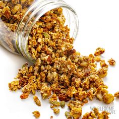 a glass jar filled with granola sitting on top of a white table next to a pile of nuts