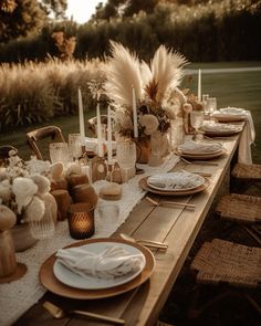 an outdoor table set with plates, candles and vases on top of the table